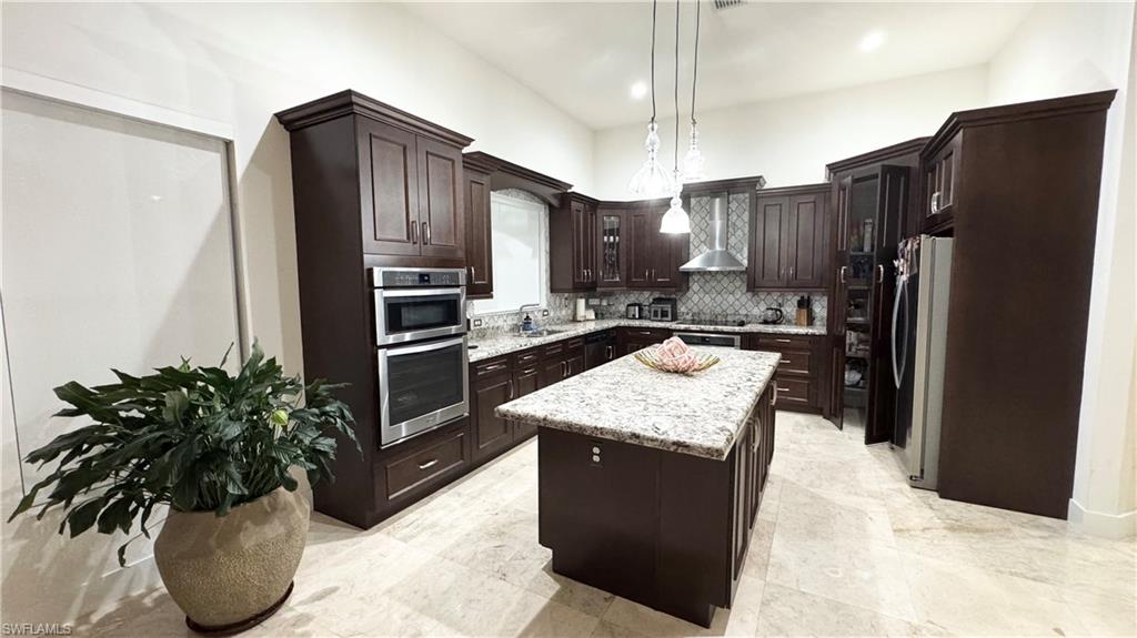 5340 Allen Place Ave Maria, FL 34142 - Photo 3 of 35 Kitchen with dark brown cabinets, wall chimney exhaust hood, stainless steel appliances, a kitchen island, and hanging light fixtures
