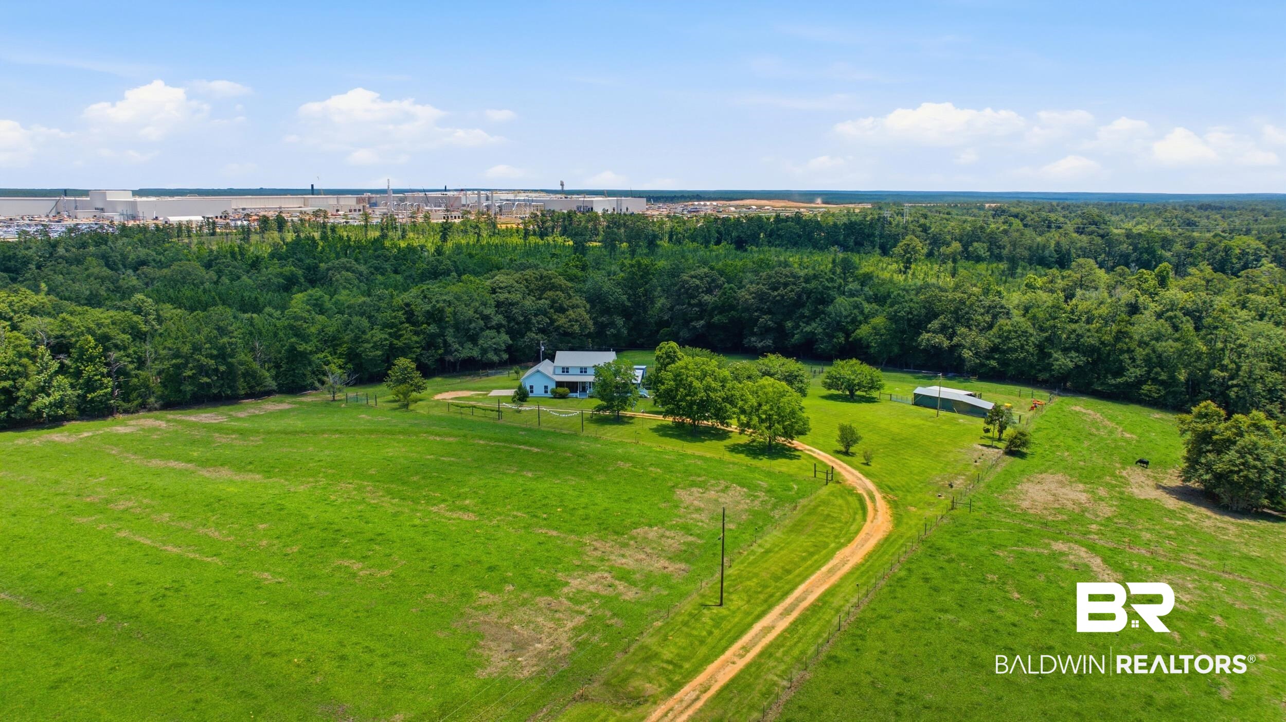 15855 Calvin Richerson Road Bay Minette, AL 36507 - Photo 61 of 83 Expansive green field featuring a winding dirt road, mature trees, and a distant blue residence with a white porch
