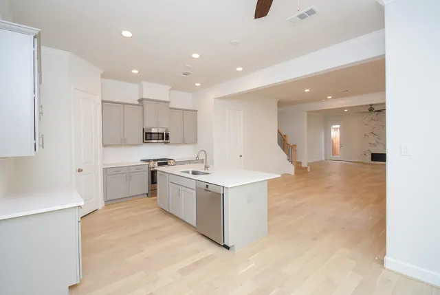 a large kitchen with a large counter top a sink stainless steel appliances and cabinets
