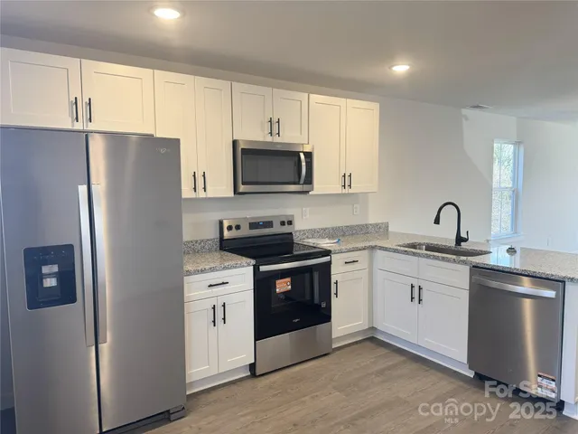 a kitchen with stainless steel appliances granite countertop white cabinets a sink a stove a refrigerator and microwave with wooden floor