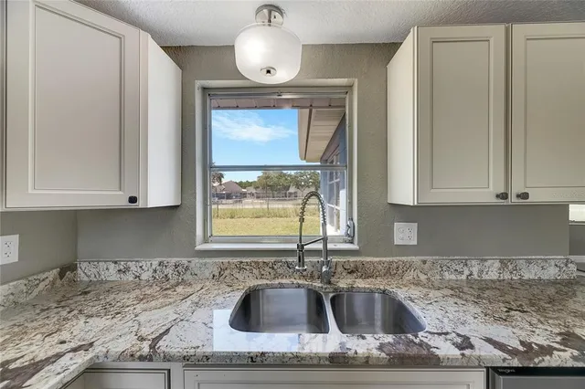 a kitchen with granite countertop a sink window and cabinets