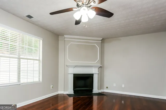 a view of an empty room with wooden floor a fireplace and a window