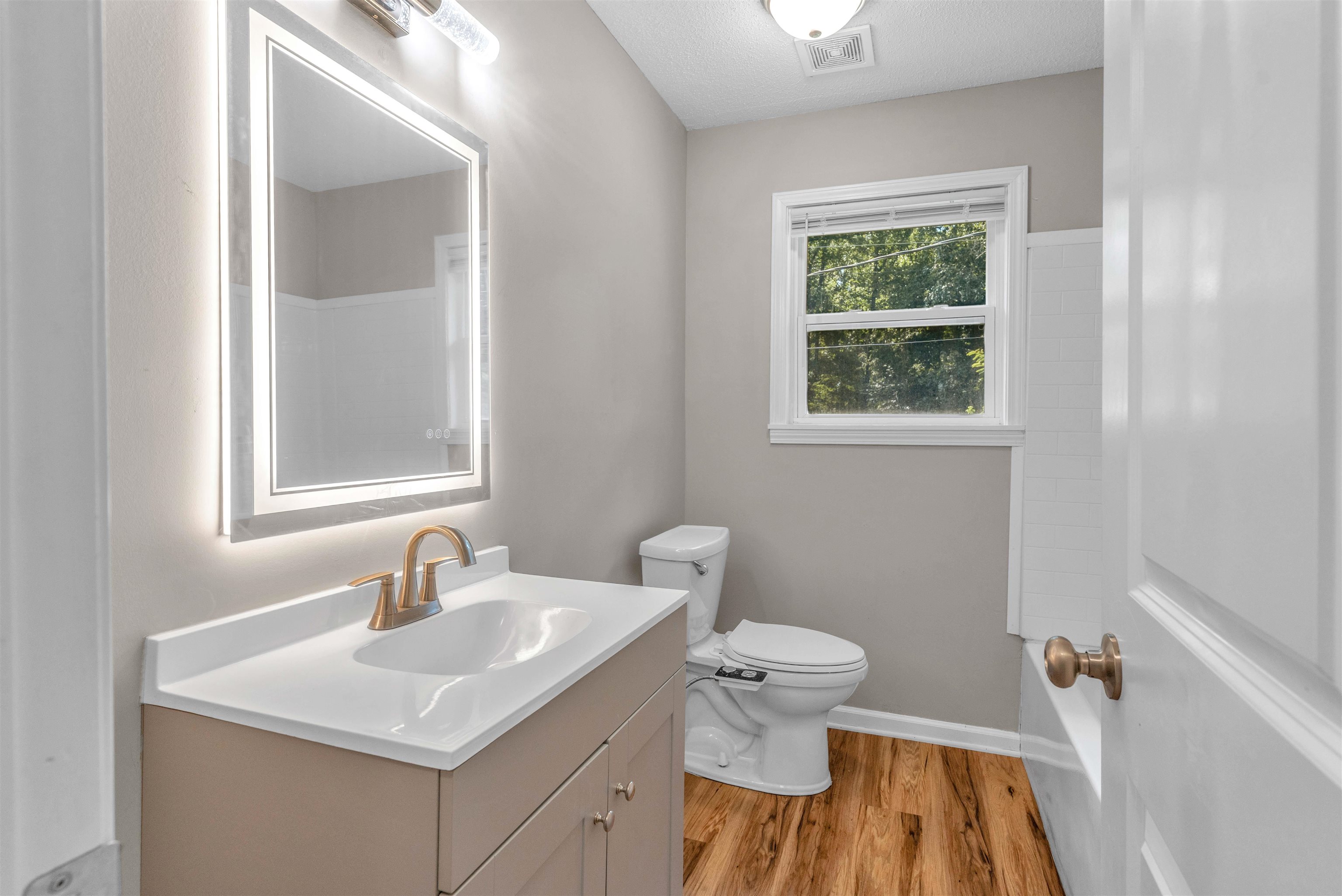 185 Henry Road Somerville, TN 38068 - Photo 13 of 21 Vanity with integrated sink and brass-finish faucet, LED-backlit mirror, wood-finish flooring, and a double-hung window