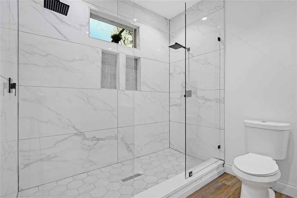 2606 Fordham Road Dallas, TX 75216 - Photo 6 of 19 Shower enclosure featuring a frameless glass door, white marble-look tile walls, hexagonal tile floor, and black rain shower head