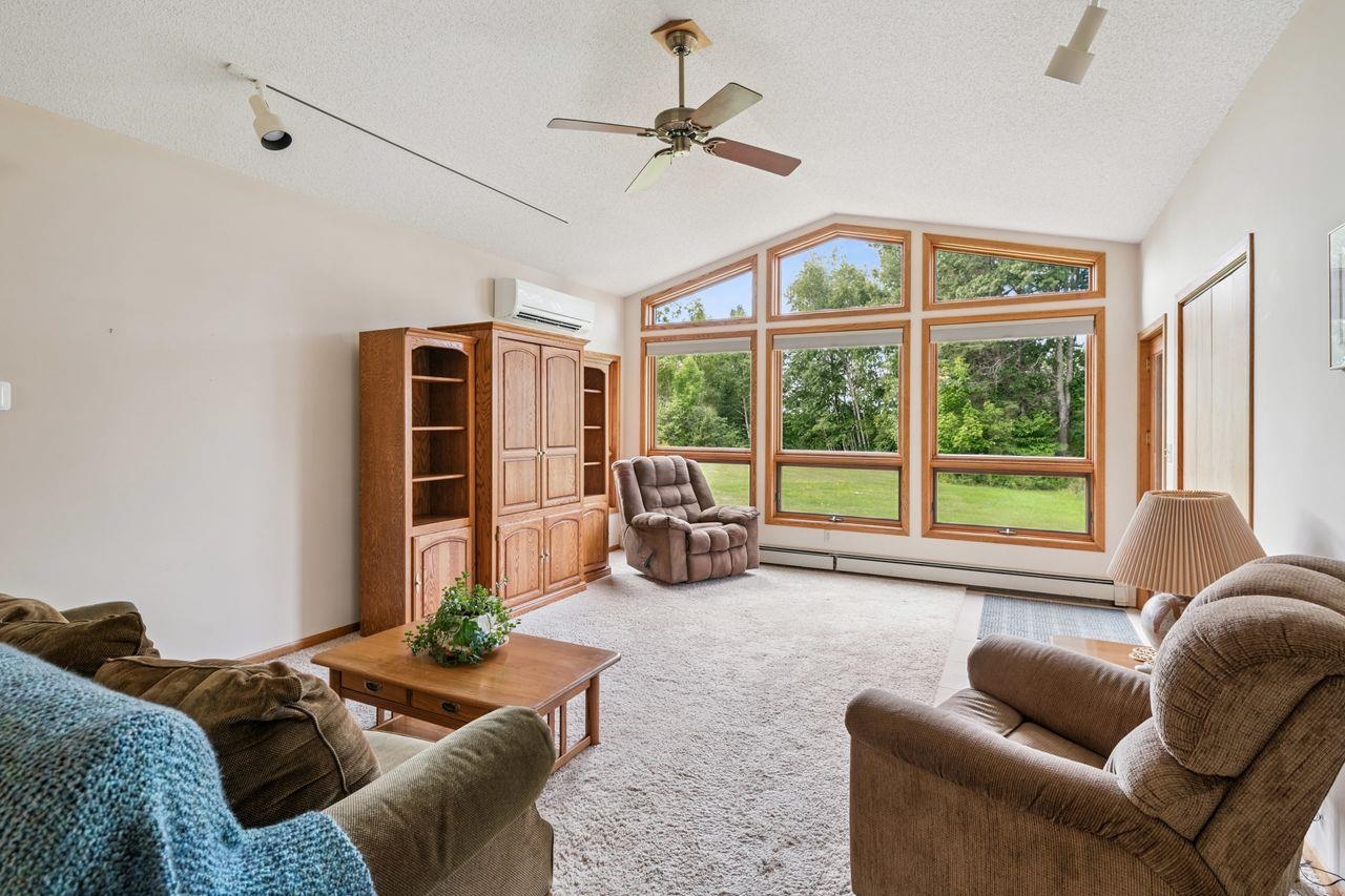 75920 Ondossagon Road Washburn, WI 54891 - Photo 3 of 29 Living room featuring lofted ceiling, light carpet, a baseboard heating unit, a textured ceiling, and an AC wall unit