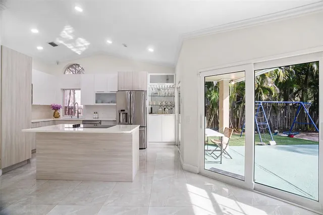 a view of kitchen with stainless steel appliances kitchen island granite countertop a refrigerator a sink a stove and white cabinets with wooden floor