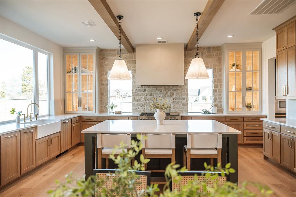 Kitchen with beamed ceiling, a kitchen island, decorative backsplash, light stone counters, and two tone cabinetry