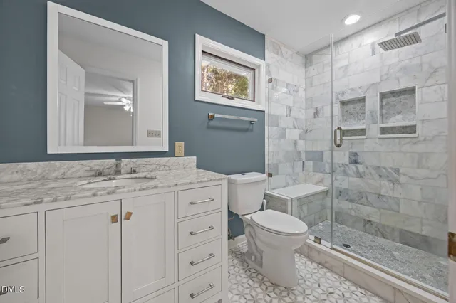 a bathroom with a granite countertop toilet a sink a mirror a window and a shower