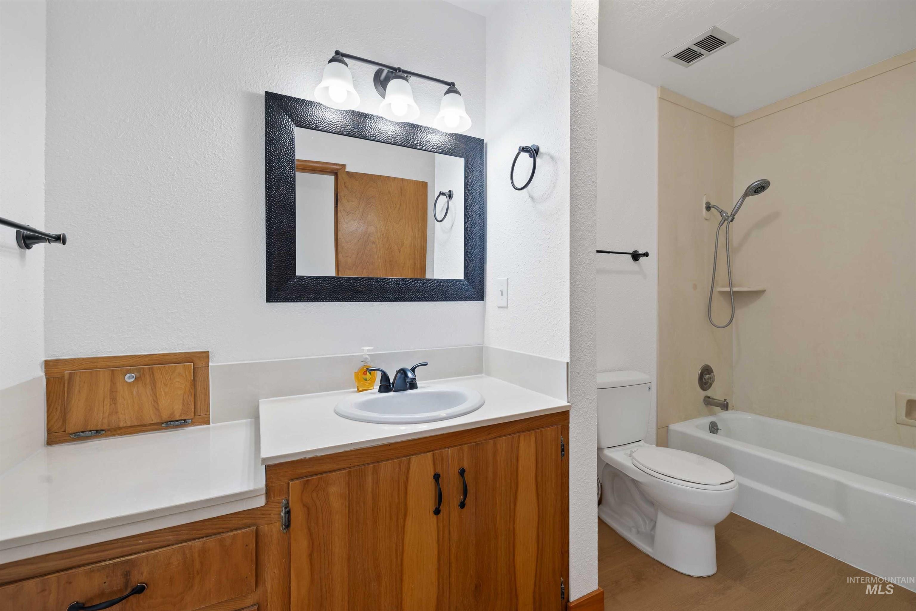 321 Clear Lakes Road Buhl, ID 83316 - Photo 13 of 34 White vanity countertop with integrated sink, wood-finish cabinetry, black-framed mirror, and a white bathtub with shower fixture