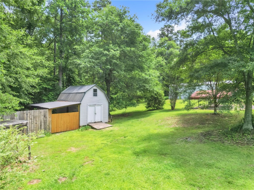 506 Charlies Creek Road Iva, SC 29655 - Photo 25 of 28 A verdant backyard retreat features a well-maintained shed with an attached covered area, surrounded by mature trees.