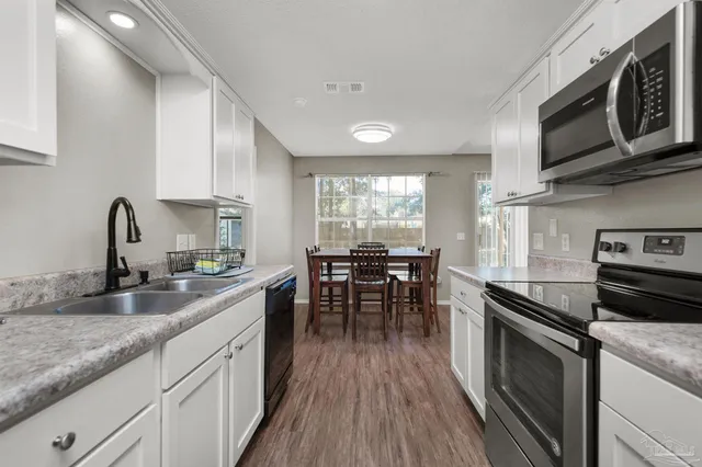 a kitchen with stainless steel appliances granite countertop a stove top oven a sink dishwasher a dining table and chairs with wooden floor