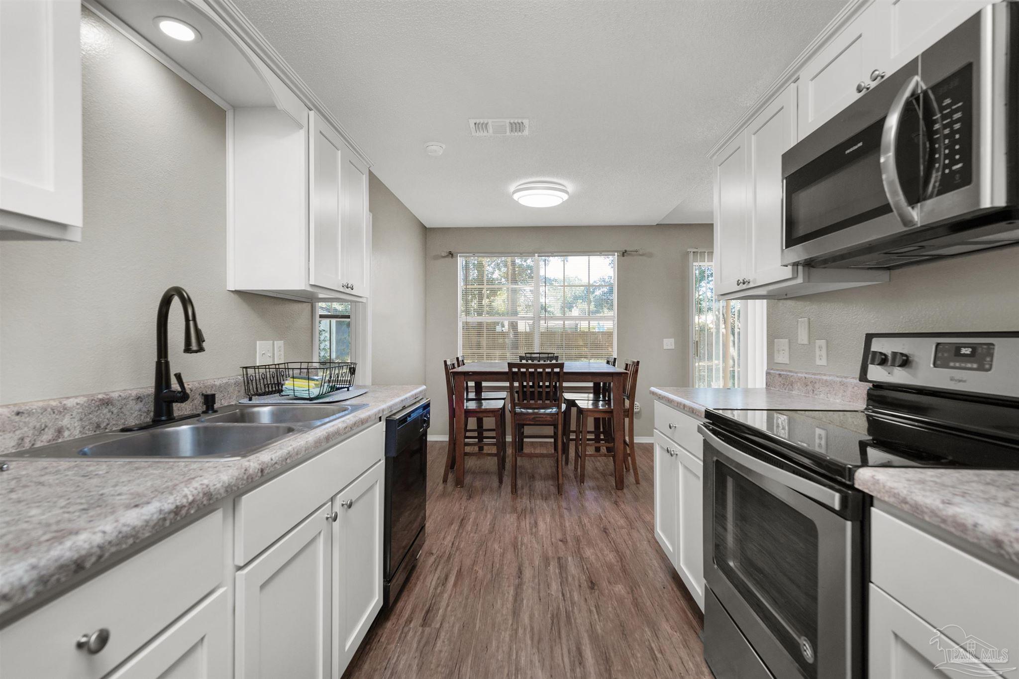 5499 Chantilly Circle Milton, FL 32583 - Photo 9 of 24 a kitchen with stainless steel appliances granite countertop a stove top oven a sink dishwasher a dining table and chairs with wooden floor