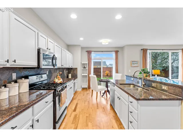 a kitchen with stainless steel appliances granite countertop a stove a sink dishwasher and a microwave oven with white cabinets