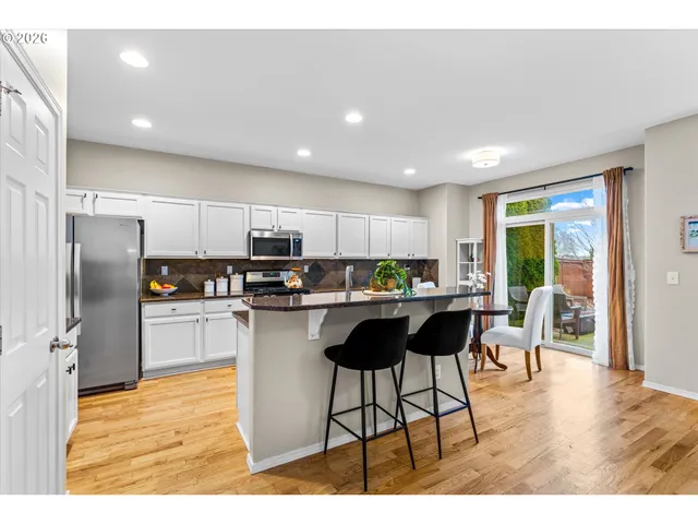 a kitchen with stainless steel appliances kitchen island granite countertop a refrigerator a stove a sink a dining table and chairs with wooden floor