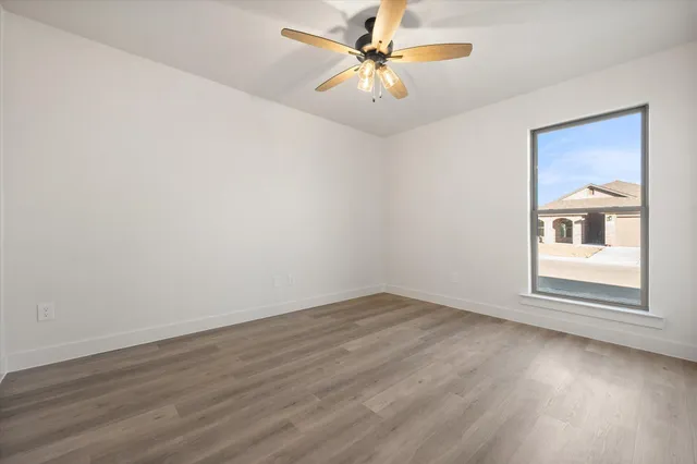 an empty room with wooden floor chandelier fan and windows