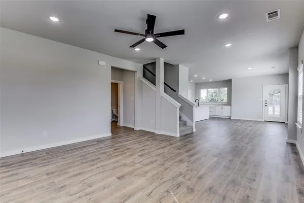 a view of an empty room with wooden floor and a ceiling fan
