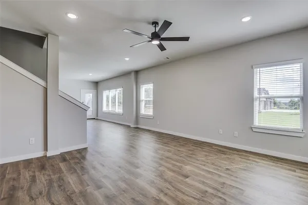 an empty room with wooden floor fan and windows