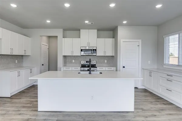 a large kitchen with stainless steel appliances granite countertop a stove a sink a refrigerator and white cabinets with wooden floor