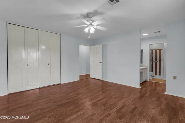 a view of an empty room with wooden floor and a ceiling fan
