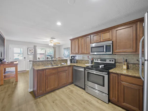 a kitchen with stainless steel appliances granite countertop a stove top oven a sink dishwasher a dining table and chairs with wooden floor