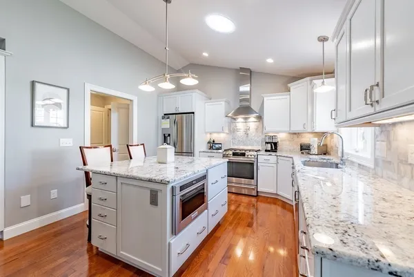 a kitchen with stainless steel appliances granite countertop a stove top oven a sink dishwasher a refrigerator and white cabinets with wooden floor