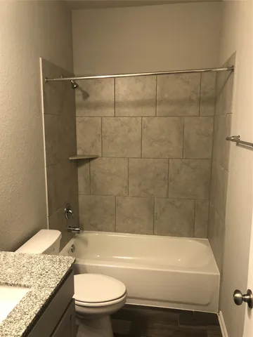 a bathroom with a granite countertop bathtub shower sink vanity and toilet