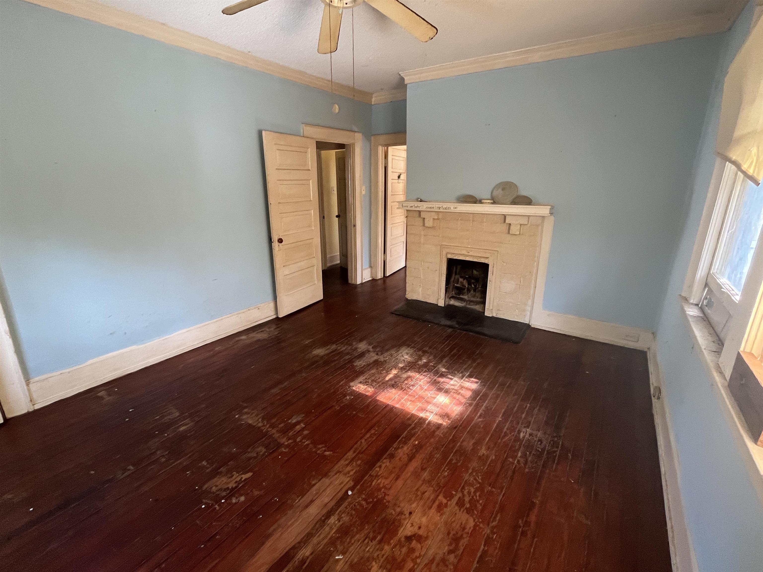 211 4th Street Mobile, AL 36611 - Photo 28 of 34 Unfurnished living room featuring dark wood finished floors, crown molding, a fireplace with raised hearth, and ceiling fan