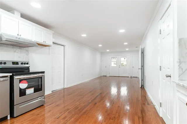 a view of an empty room with wooden floor and a kitchen