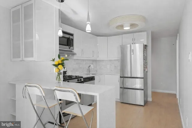 a kitchen with stainless steel appliances a refrigerator a stove a sink a dining table and chairs with wooden floor