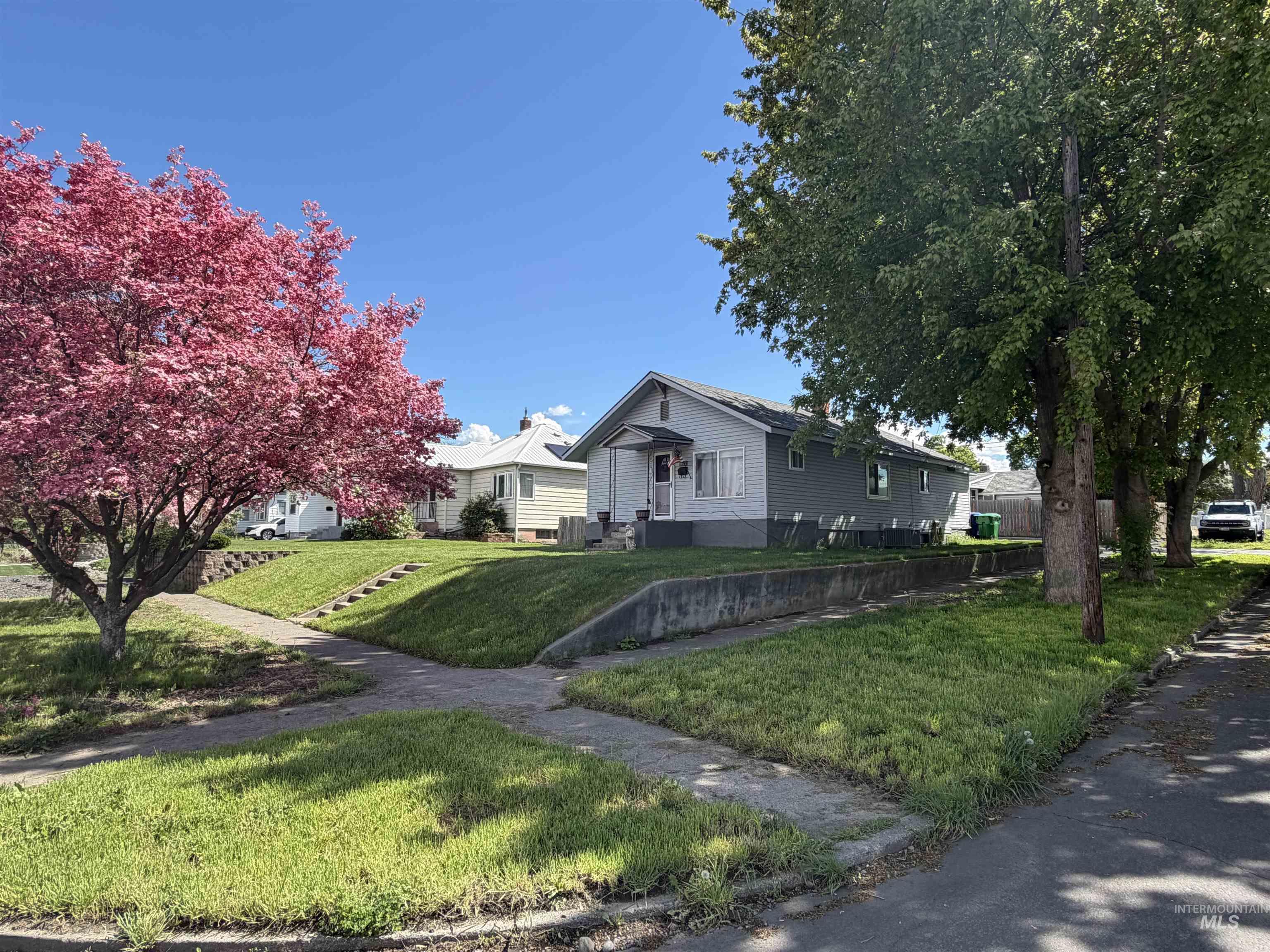 1602 14th Avenue Lewiston, ID 83501 - Photo 8 of 32 Gray siding residence with a concrete foundation, featuring a concrete walkway, established front lawn, and mature trees including one with pink blossoms