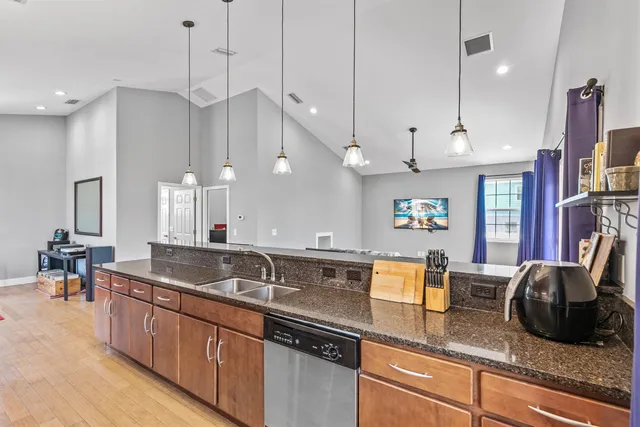 a kitchen with stainless steel appliances granite countertop a refrigerator a sink dishwasher a stove and a dining table with wooden floor