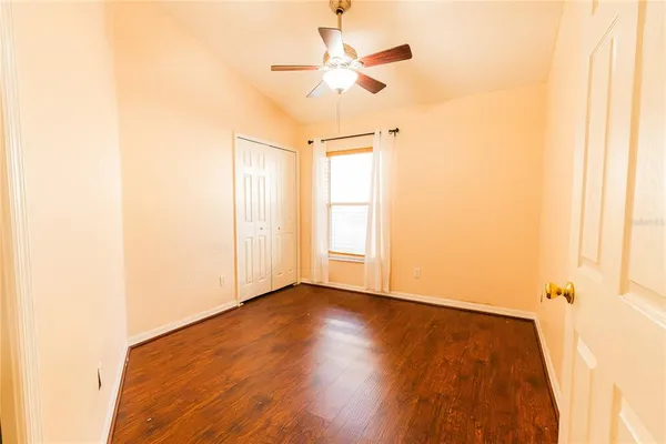 a view of an empty room with wooden floor and a ceiling fan