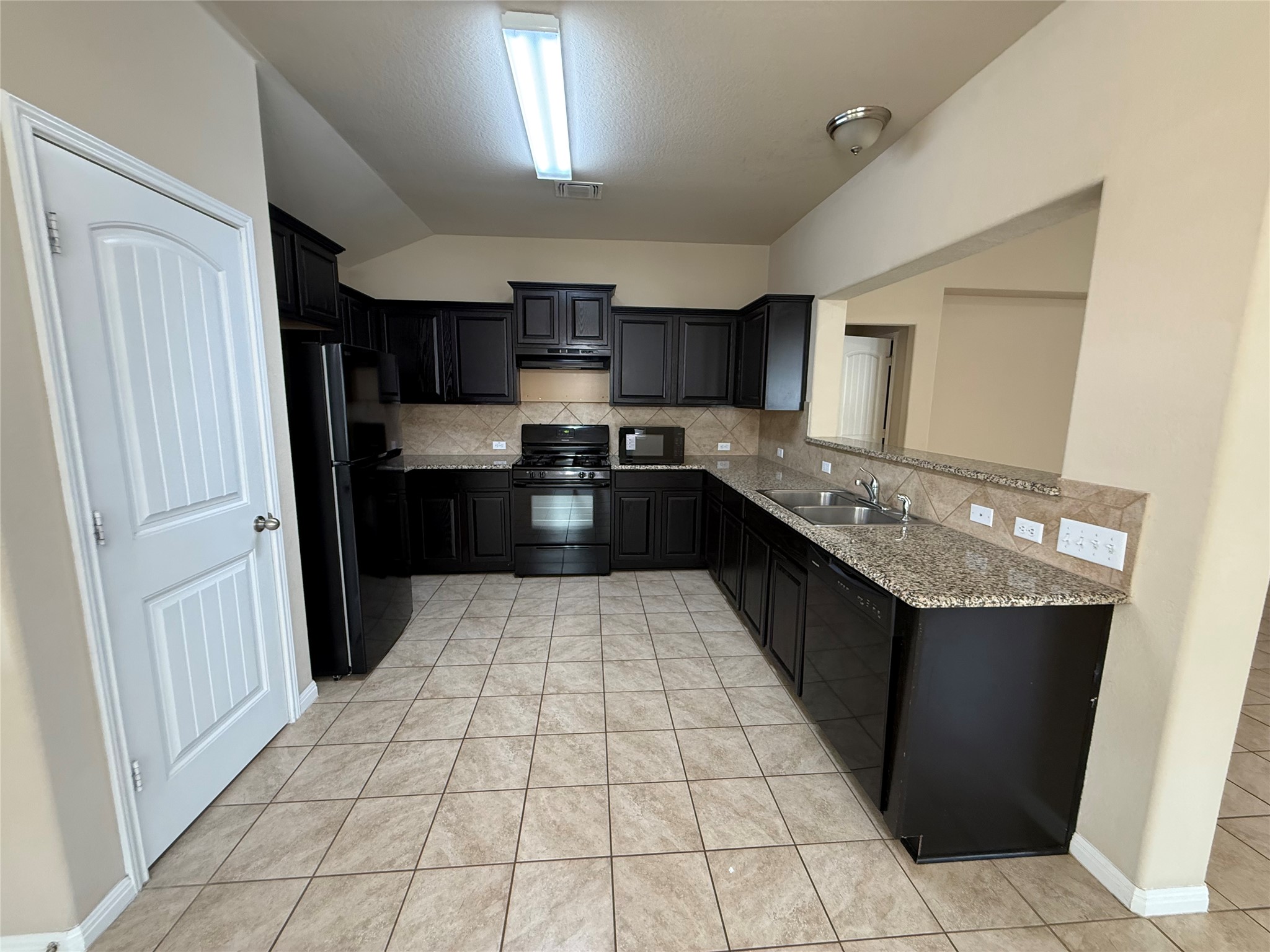 1441 Hamiltons Way Leander, TX 78641 - Photo 15 of 20 Kitchen with dark cabinetry, black appliances, tasteful backsplash, light stone counters, and lofted ceiling