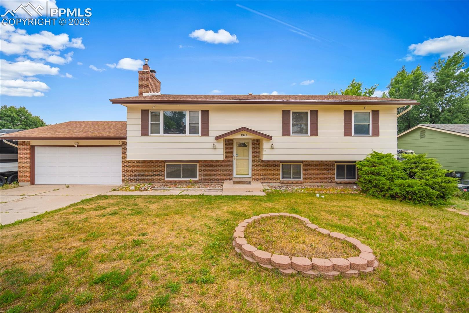 1921 Wooten Road Colorado Springs, CO 80915 - Photo 1 of 49 Raised ranch featuring a garage, a chimney, brick siding, and a front yard