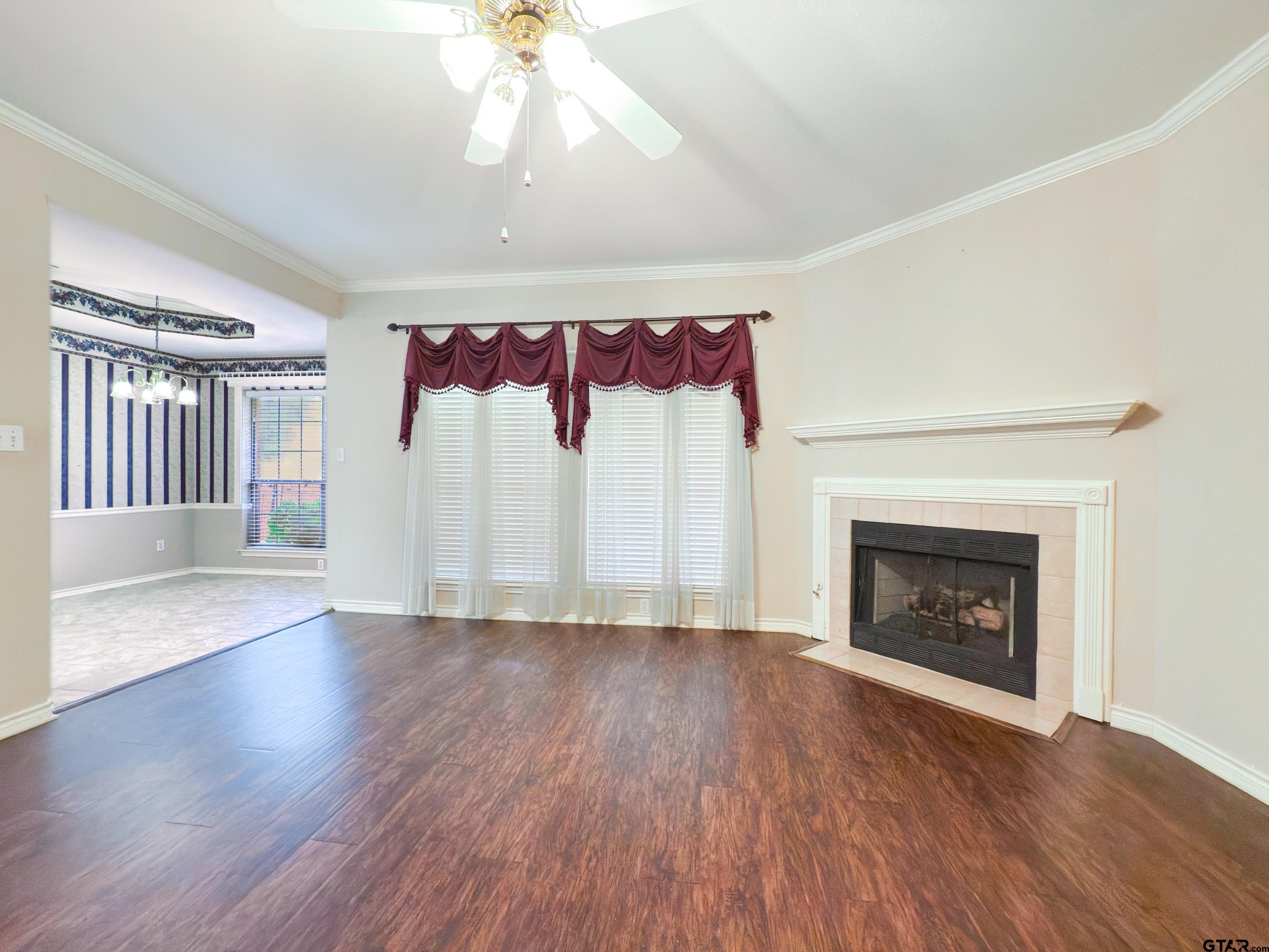 1202 Rice Road, Unit 112 Tyler, TX 75703 - Photo 2 of 12 an empty room with wooden floor chandeliers a fireplace and windows