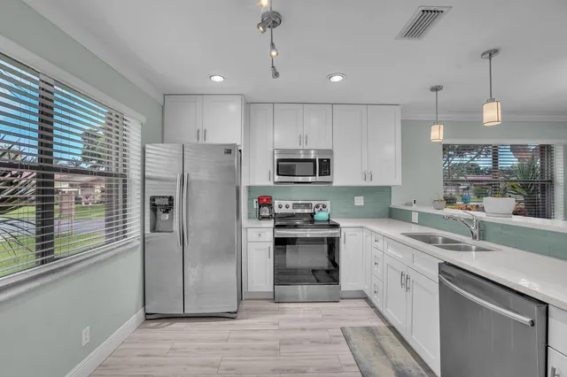 a kitchen with stainless steel appliances granite countertop a refrigerator a sink dishwasher a stove and white cabinets with wooden floor