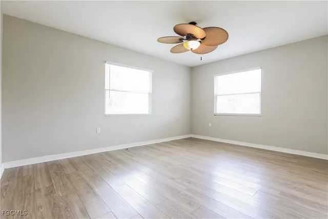 an empty room with wooden floor chandelier fan and windows