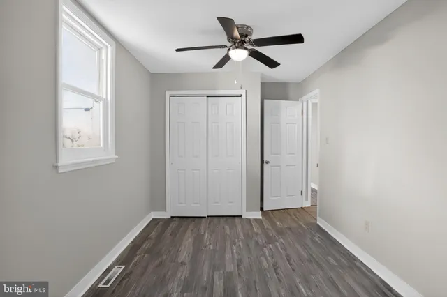 an empty room with wooden floor ceiling fan and windows