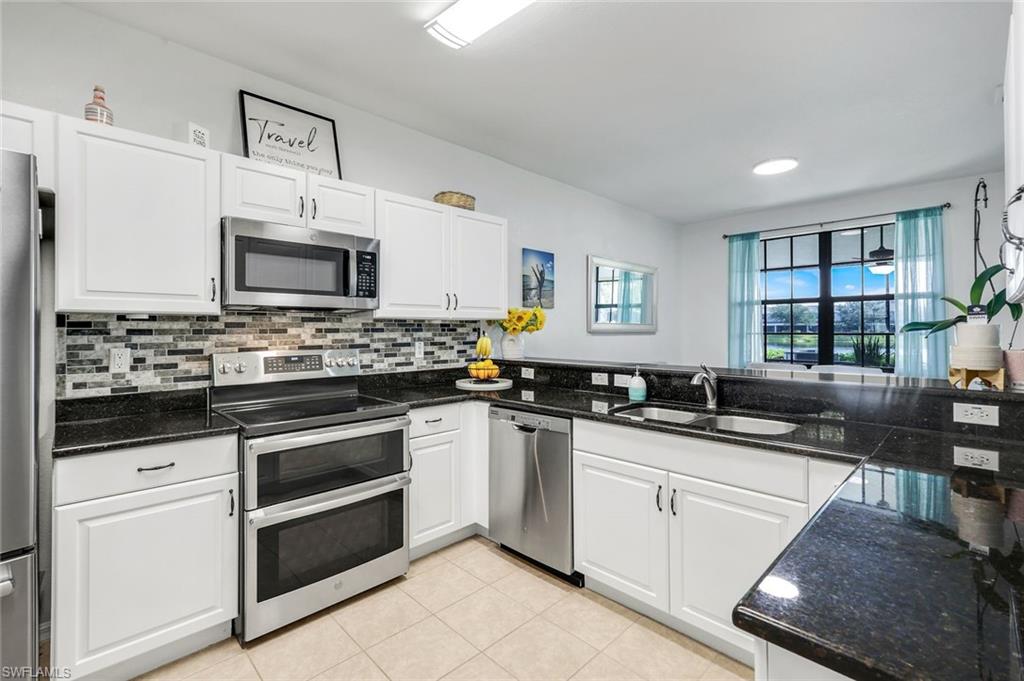 15239 Summit Pl Circle, Unit 246 Naples, FL 34119 - Photo 15 of 49 Kitchen with stainless steel appliances, white cabinets, backsplash, light tile patterned floors, and dark stone countertops