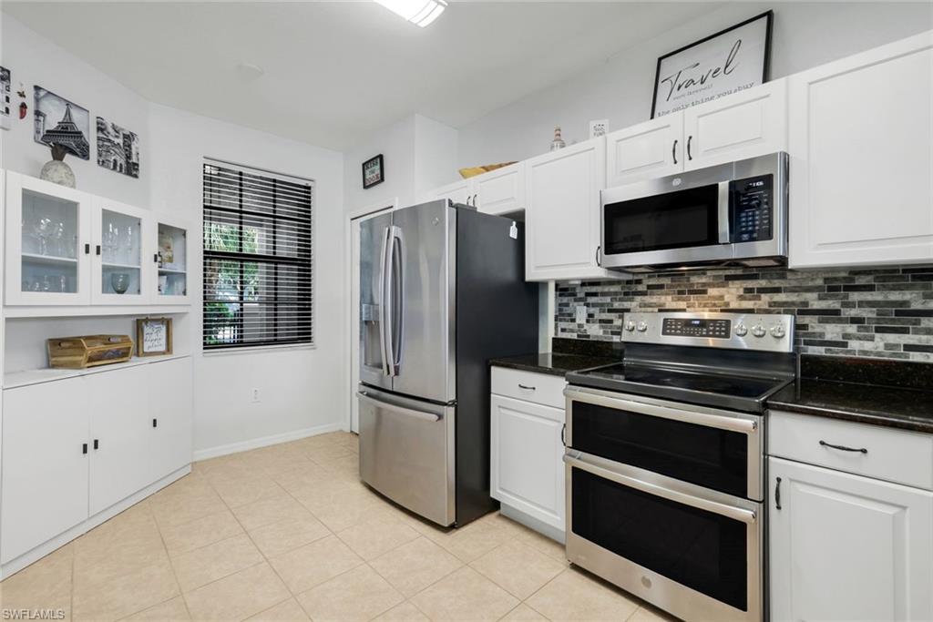 15239 Summit Pl Circle, Unit 246 Naples, FL 34119 - Photo 16 of 49 Kitchen with stainless steel appliances, glass insert cabinets, white cabinetry, decorative backsplash, and light tile patterned flooring