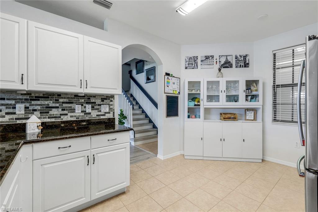 15239 Summit Pl Circle, Unit 246 Naples, FL 34119 - Photo 17 of 49 Kitchen with white cabinetry, dark stone counters, freestanding refrigerator, decorative backsplash, and light tile patterned floors