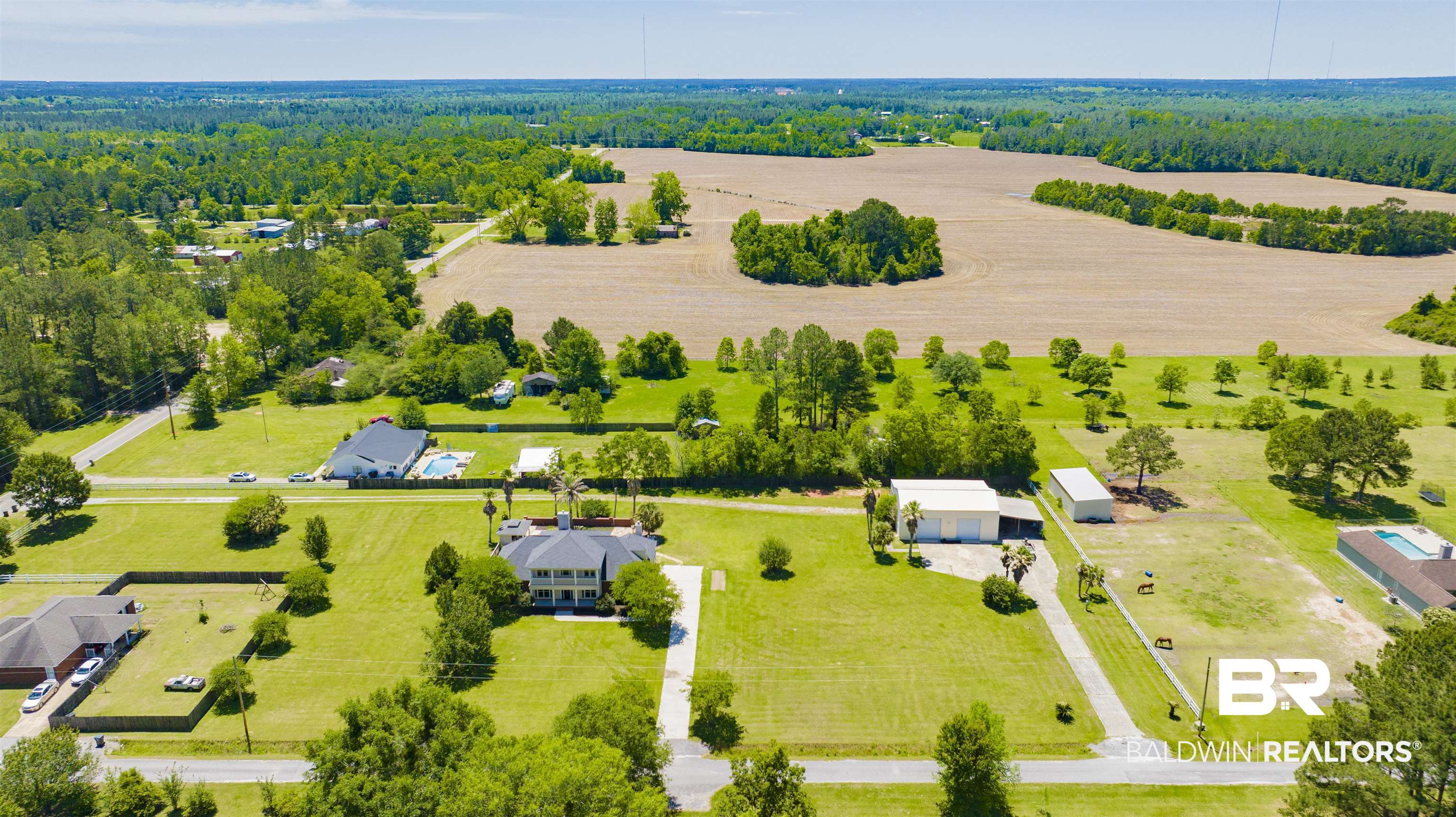 12944 Anna's Way Stapleton, AL 36578 - Photo 6 of 64 Expansive property featuring a large residence with a dark roof, a separate white outbuilding, extensive manicured green lawns, mature trees, and agricultural fields in the distance
