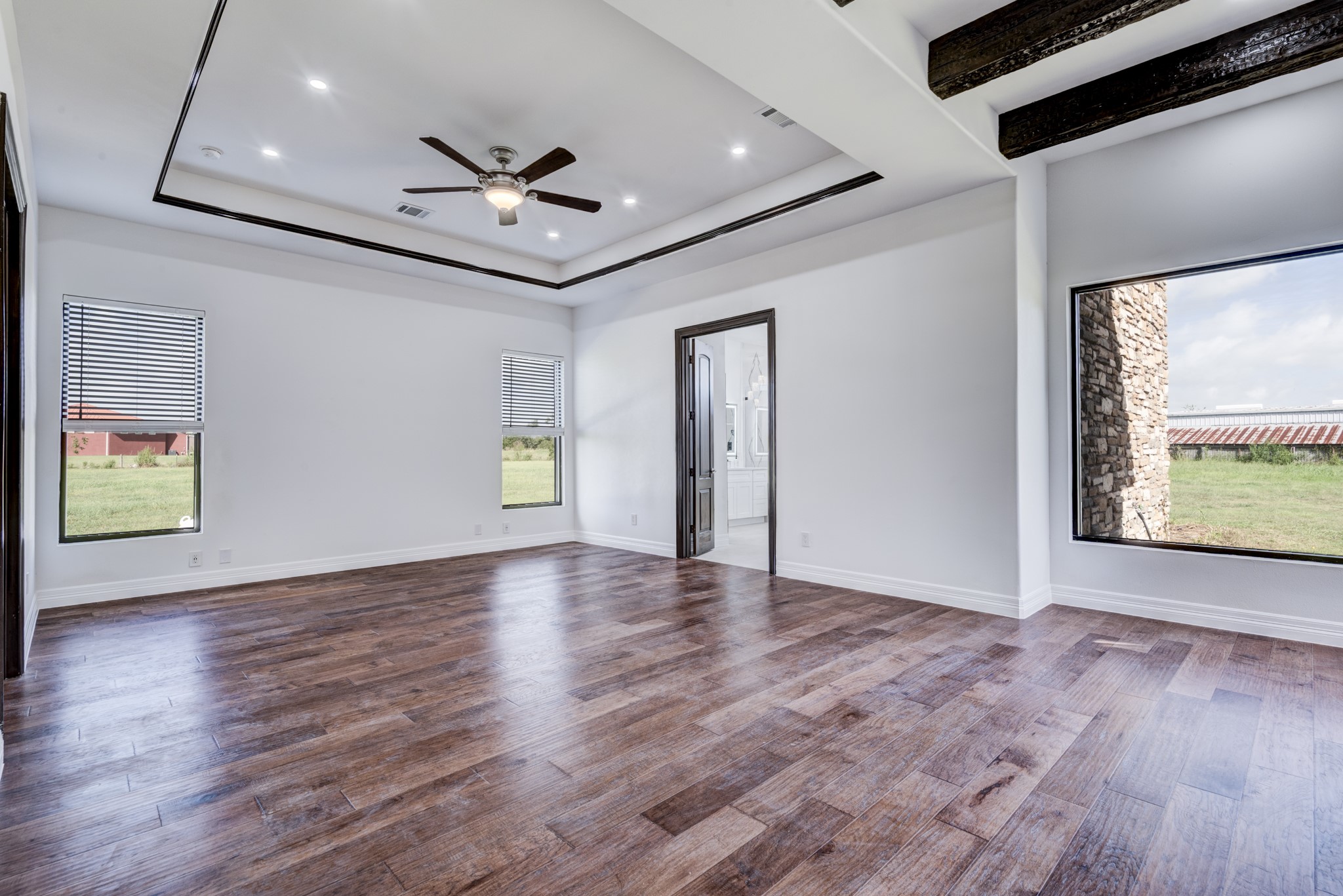 7348 Love Road Fulshear, TX 77441 - Photo 30 of 48 Experience luxury in this expansive master bedroom, featuring elegant wood floors, a stylish tray ceiling with recessed lighting, and large windows that invite natural light and serene views.