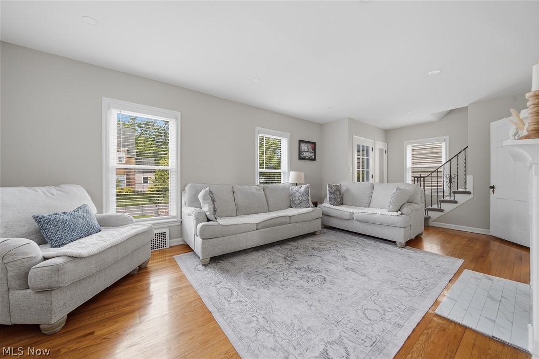 2231 Brockway Road University Heights, OH 44118 - Photo 5 of 46 Bright living area featuring hardwood flooring, multiple windows, a white fireplace with a tiled hearth, and a staircase with an iron railing