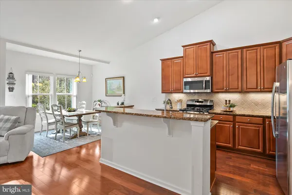 a kitchen with stainless steel appliances granite countertop a sink a stove and a living room view