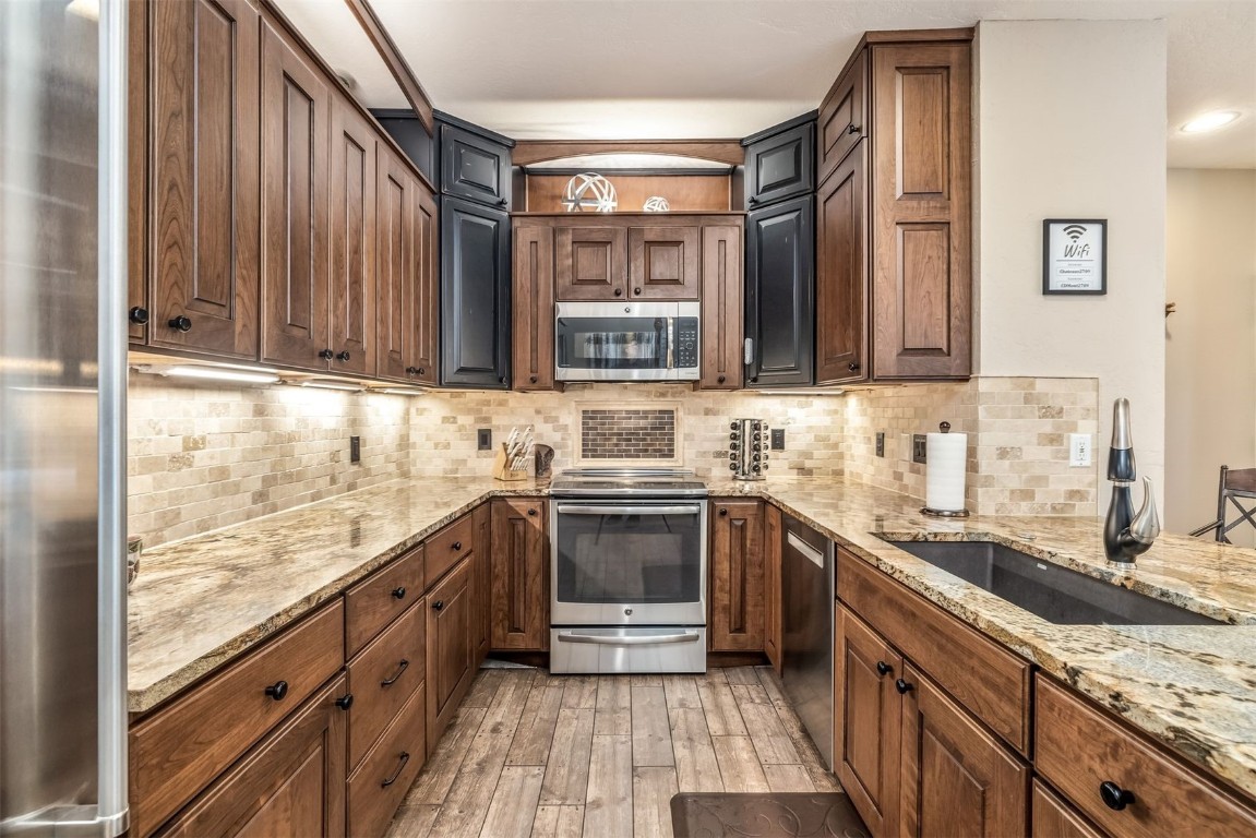 Kitchen featuring a sink, appliances with stainless steel finishes, light wood-style floors, backsplash, and light stone counters