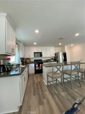 a kitchen with stainless steel appliances kitchen island granite countertop a stove top oven a sink a dining table and chairs with wooden floor