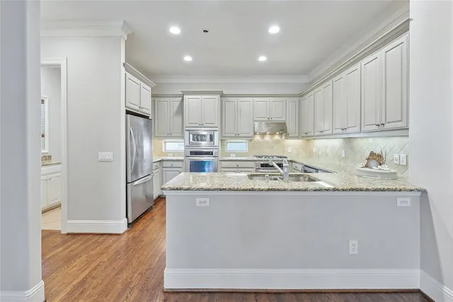 a kitchen with stainless steel appliances granite countertop a refrigerator a sink a stove and white cabinets with wooden floor