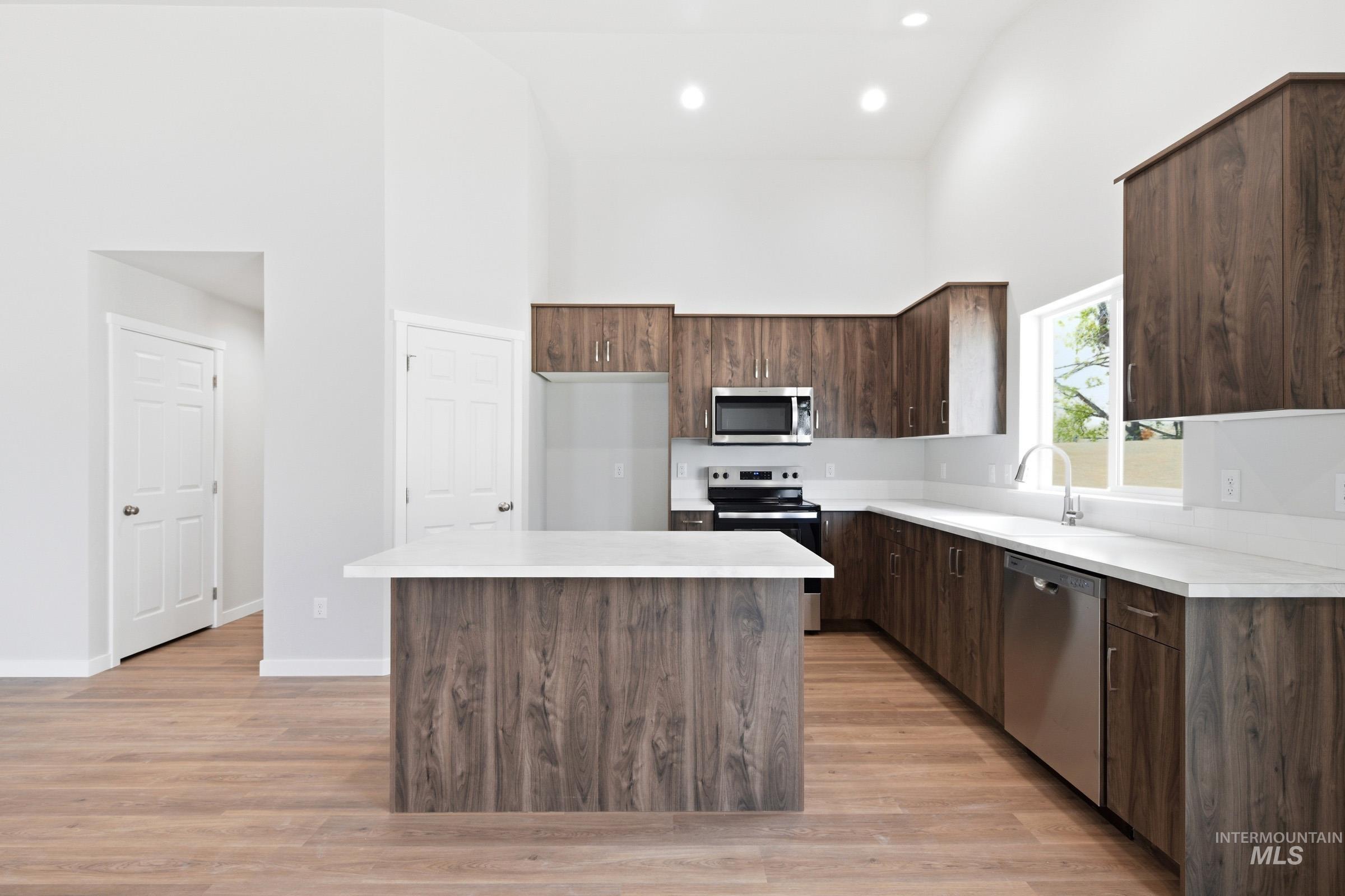 13734 Redway Court Caldwell, ID 83607 - Photo 4 of 20 Kitchen featuring light countertops, dark wood finish cabinets, stainless steel appliances, a high ceiling, and a kitchen island