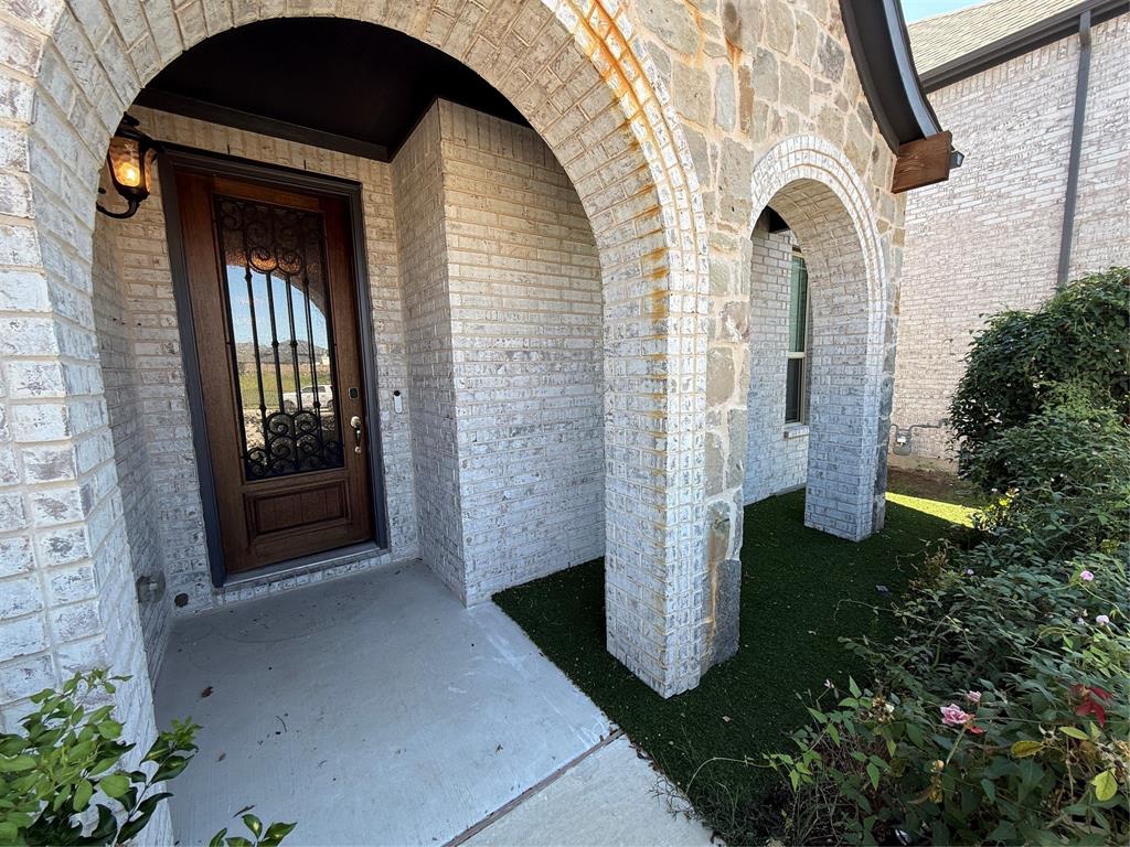 5212 Troupe Road McKinney, TX 75071 - Photo 2 of 38 Arched stone and brick entry featuring a dark wood door with wrought iron detailing and a built-in light fixture